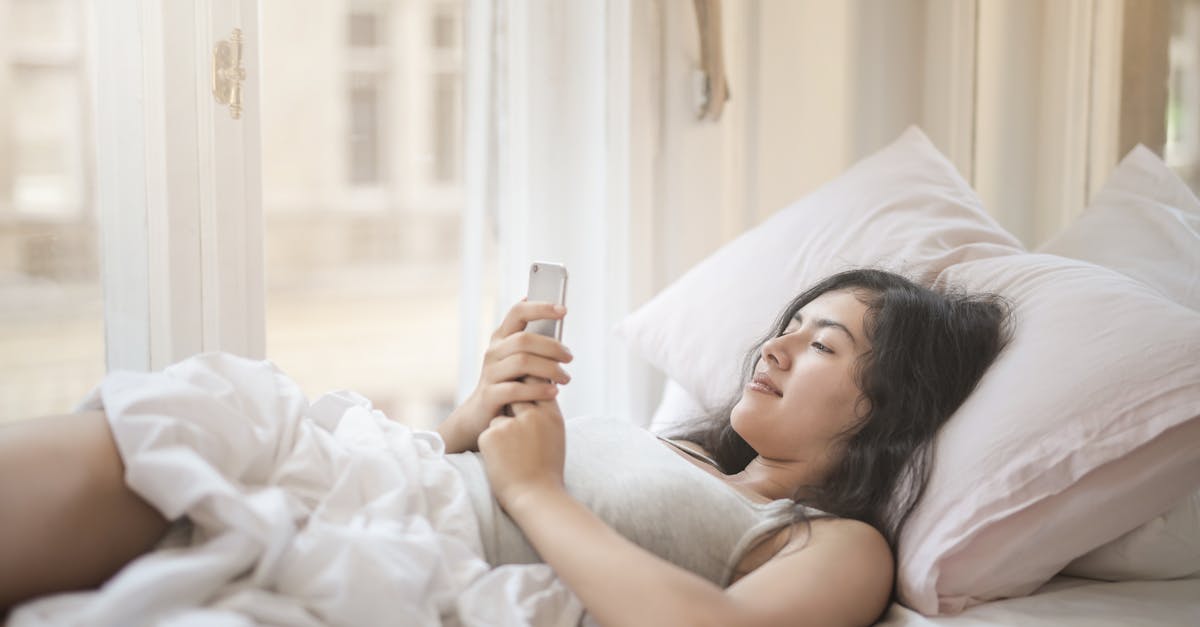 Woman enjoying a peaceful morning in bed, using her smartphone by a sunlit window